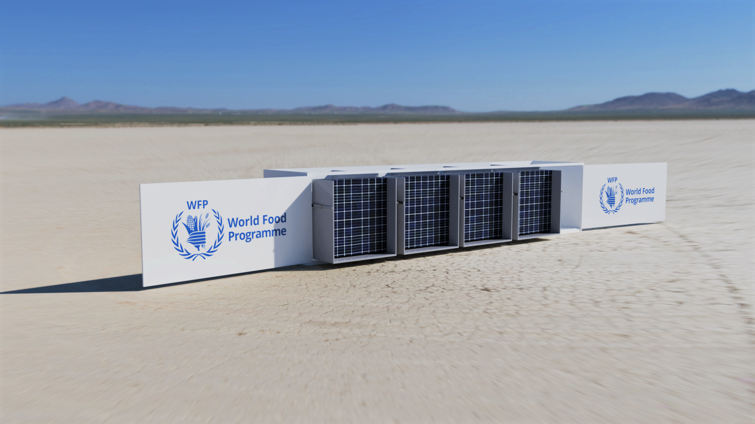 A long, white piece of modular equipment, possibly a solar-powered water generator, sits in the middle of a vast, cracked-earth desert. Large white panels on either side of the central unit are printed with the blue logo of the WFP (World Food Programme). In the background, a distant mountain range is visible under a clear blue sky.